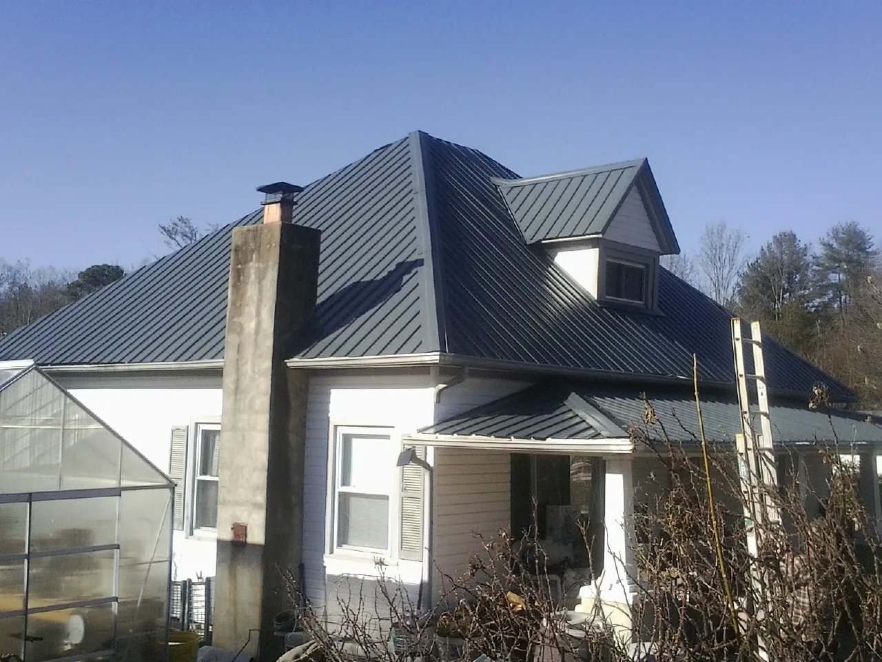 Dark blue standing seam metal roof on a white farmhouse with dormer — Slate & Tile Roof Repair by Roofing Brothers in Vergas
