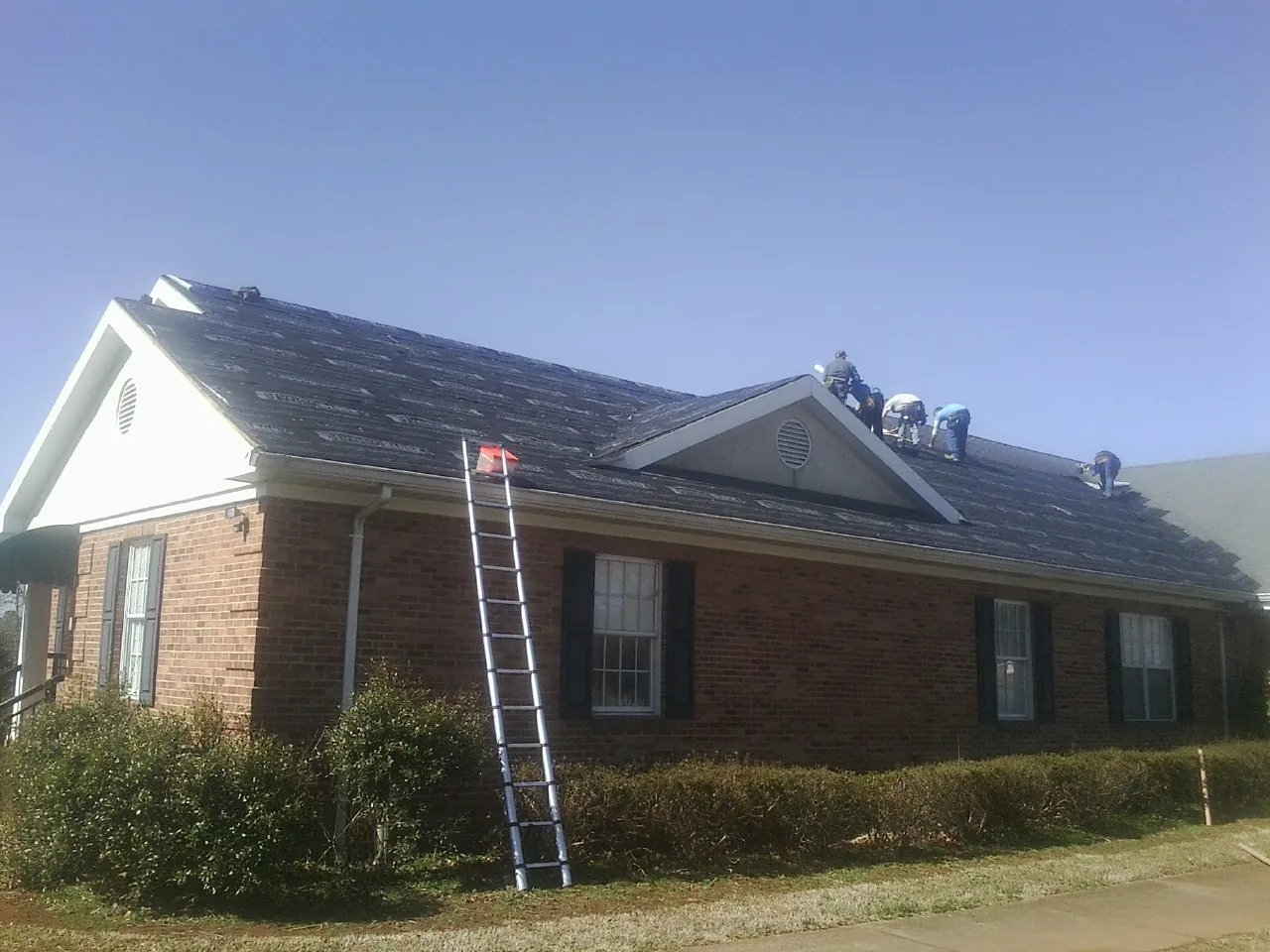 Crew tearing shingles off a brick ranch roof with a ladder set — Emergency Roof Repair work by our crew in Vergas