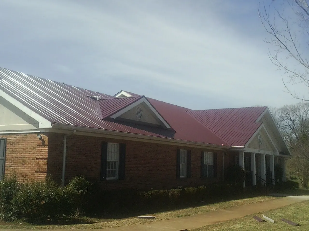 Red metal roof with gabled entries on a long brick building, from a Hail Damage Roof Repair job in Vergas