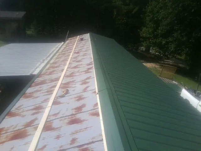 Old rusted panels beside newly installed green metal roofing — Wind Damage Roof Repair by Roofing Brothers in Vergas