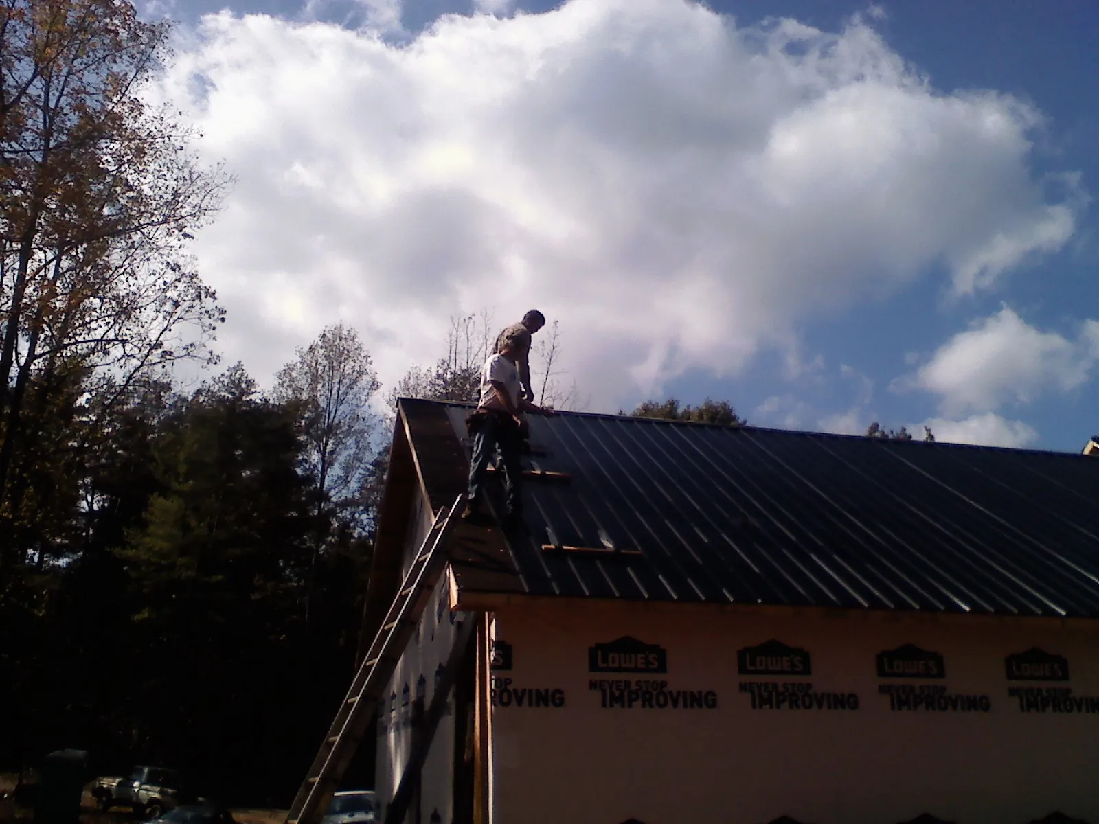 Roofer fastening dark metal panels high against a cloudy sky, from a Roof Inspection job in Vergas