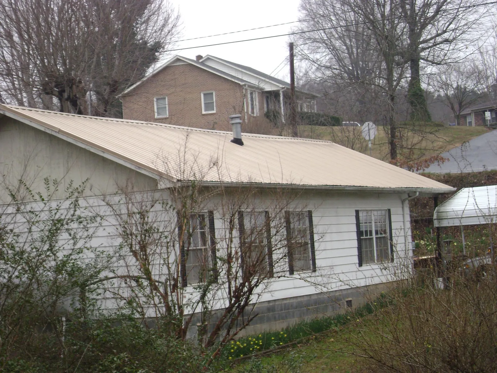 Tan metal roof on a white sided house set into a hillside — Commercial Roofing by Roofing Brothers in Vergas